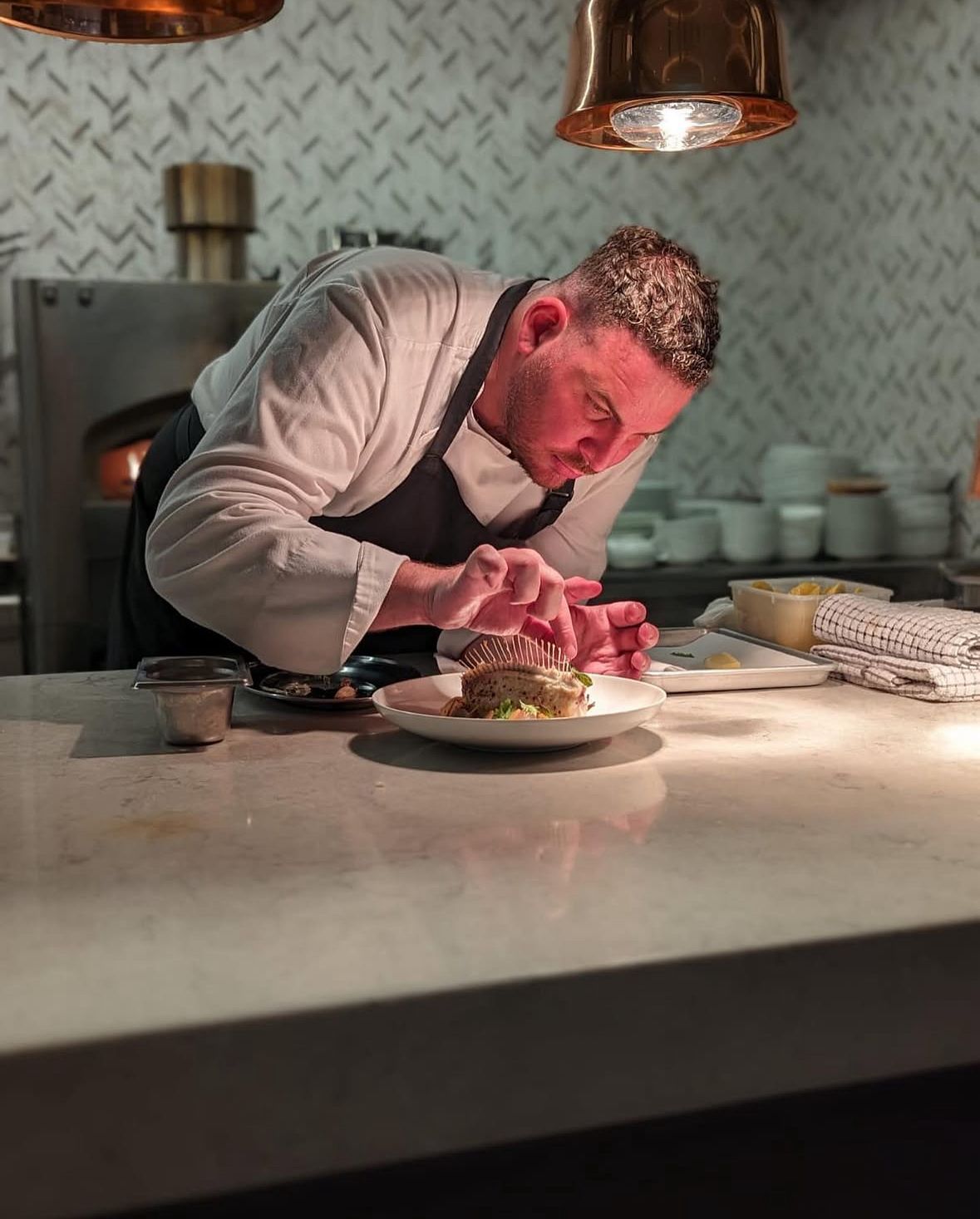 Chef Menaché Loubreaux plating a dish under copper light